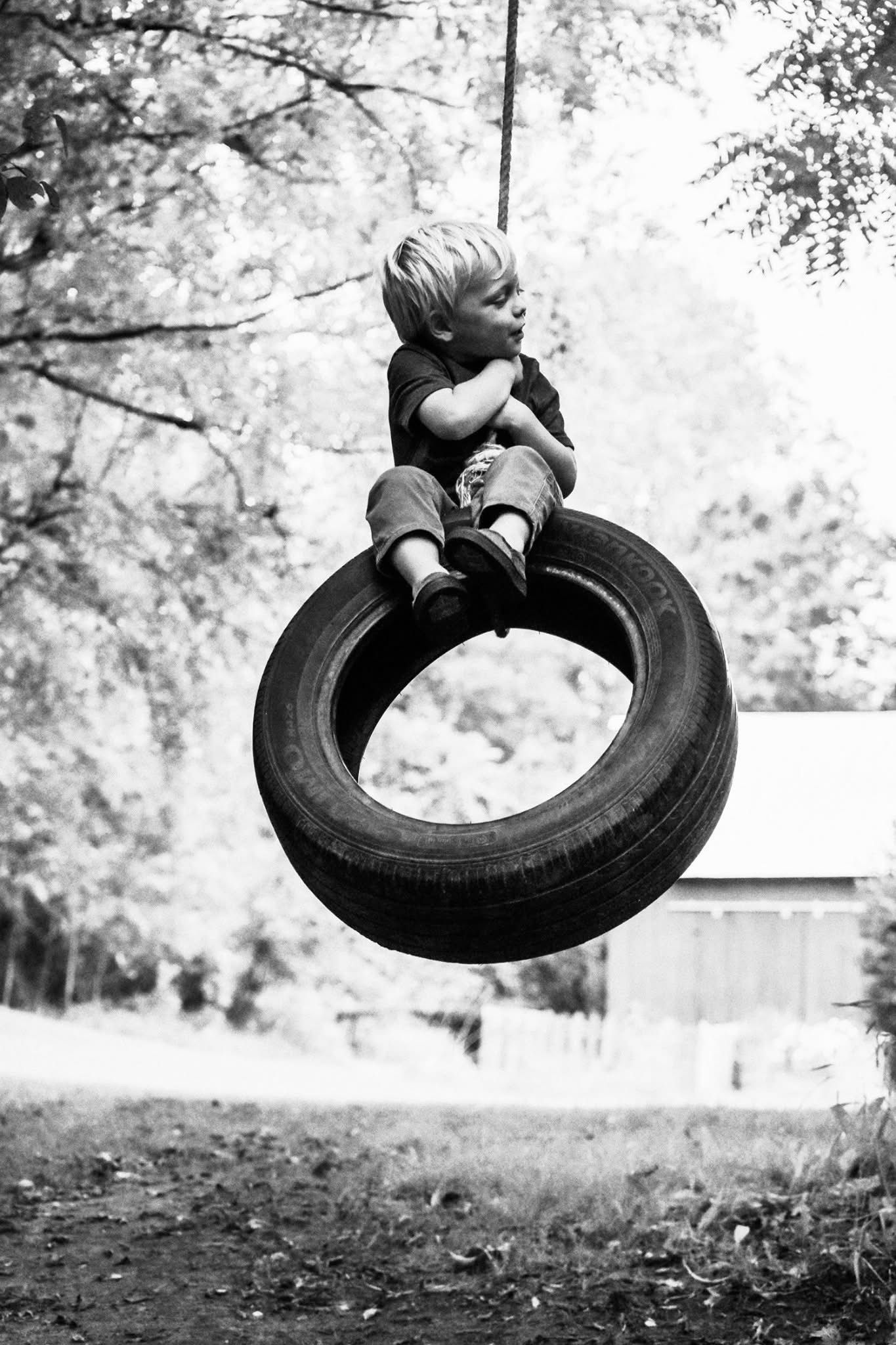 A young boy is sitting on a tire swing.