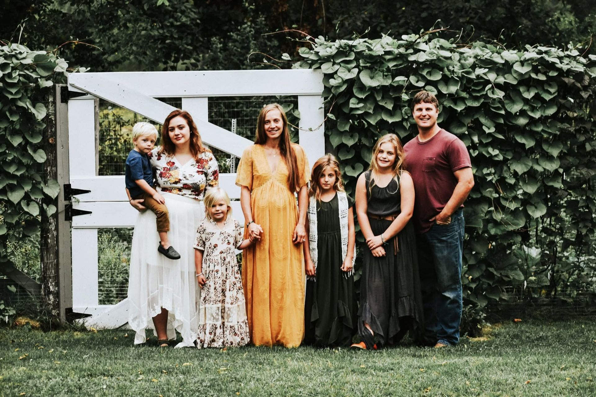 A family is posing for a picture in front of a white gate.