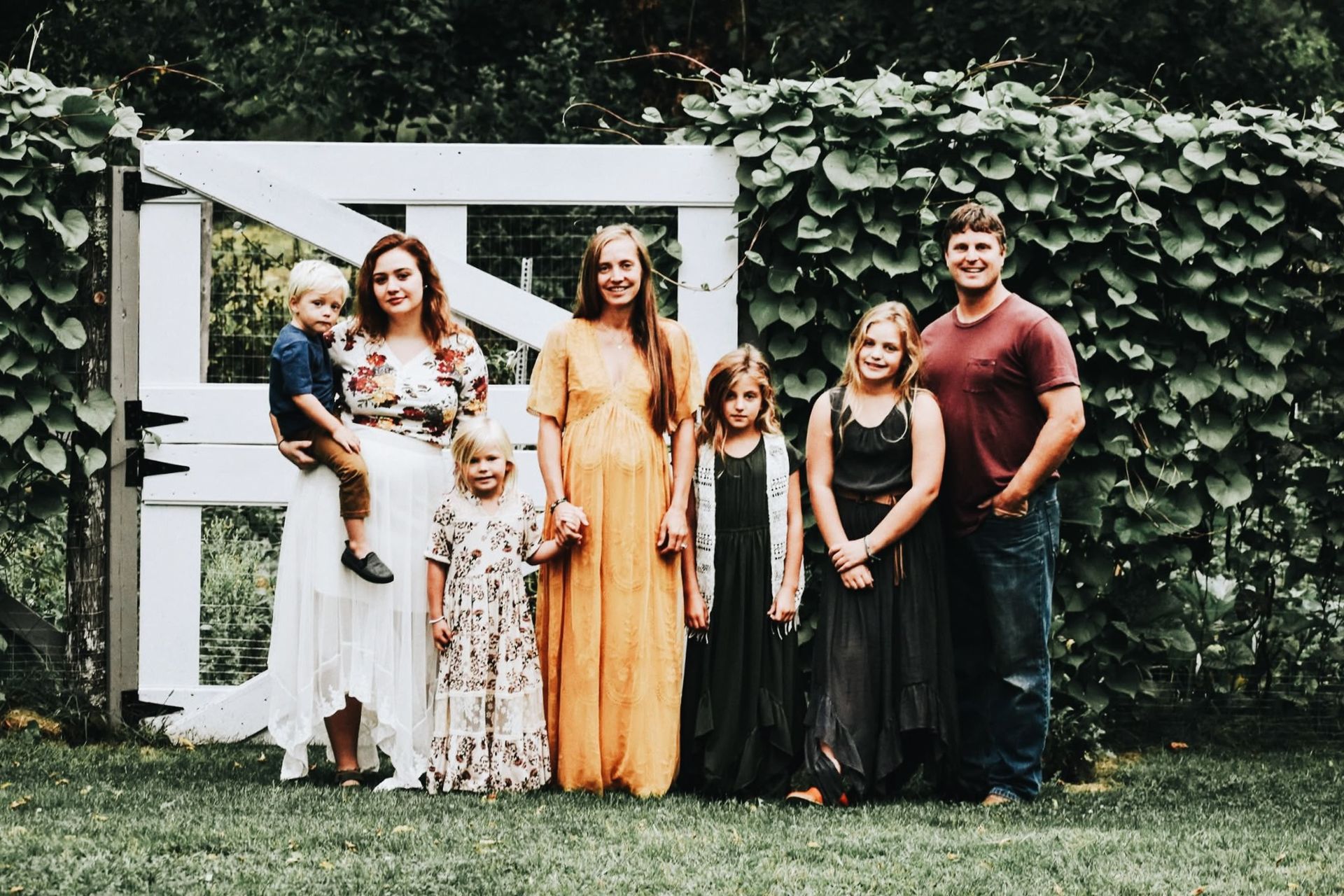 A family is posing for a picture in front of a white gate.