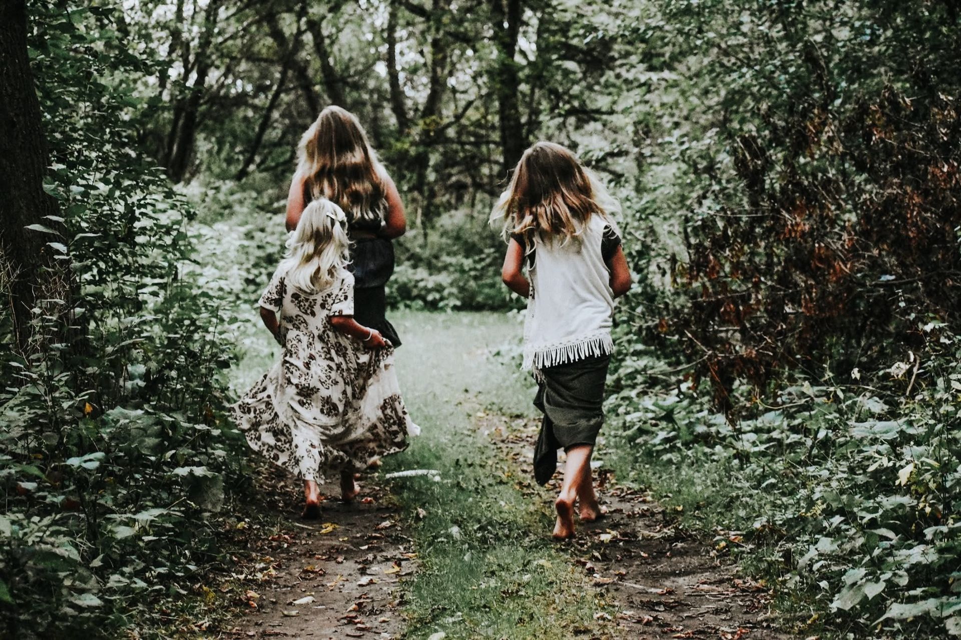 Three girls are walking down a path in the woods.