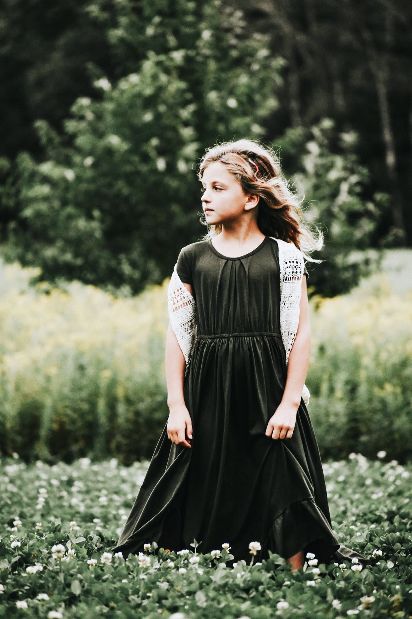 A little girl in a black dress is standing in a field of flowers.