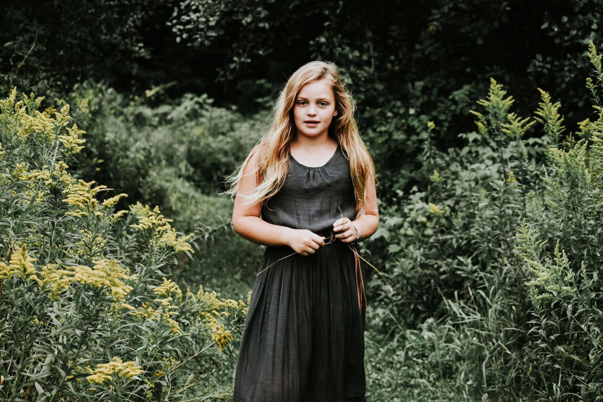 A young girl in a black dress is standing in a field.