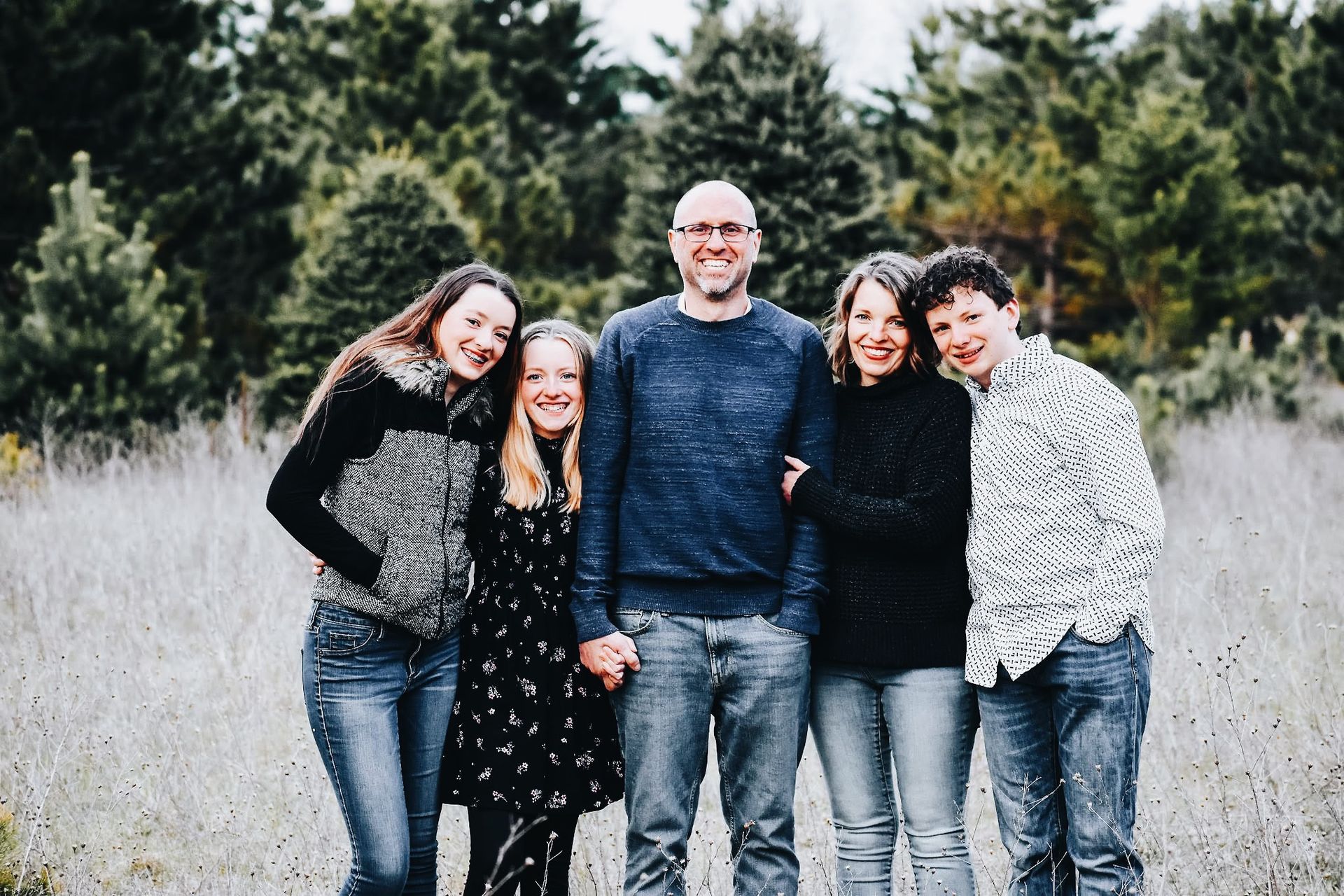A family posing for a picture in a field with trees in the background.