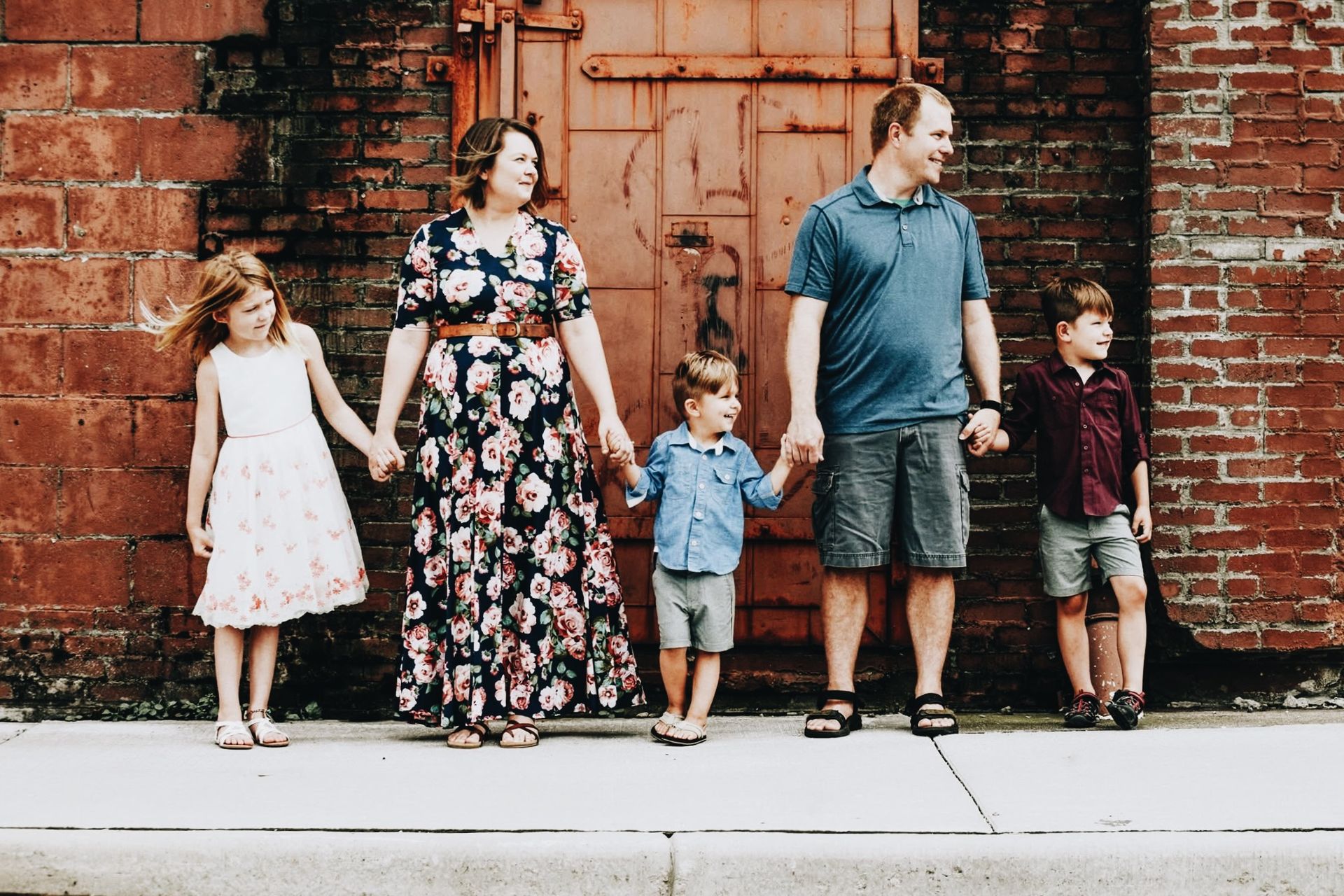 A family is standing in front of a brick wall holding hands.