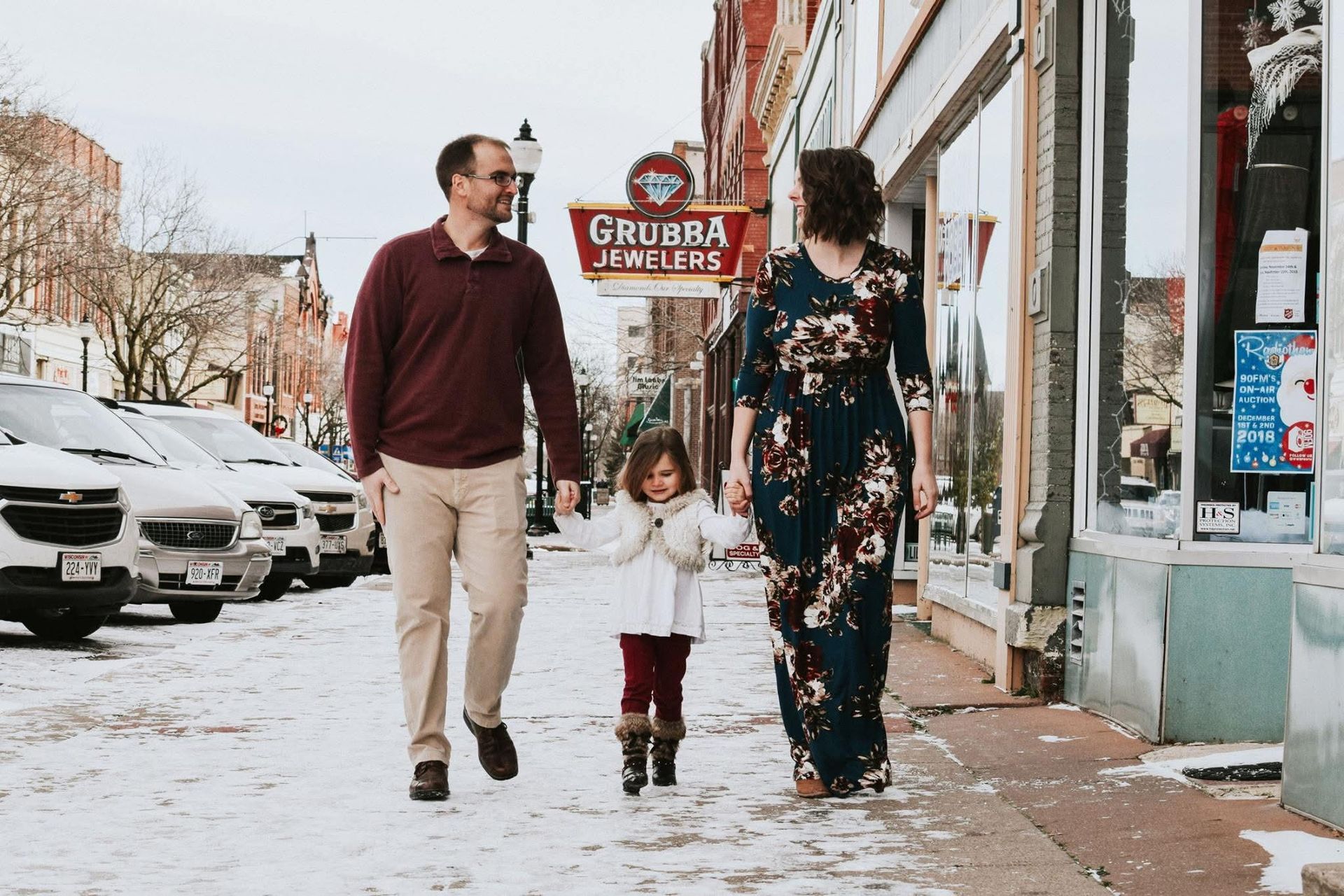 A family is walking down a snowy street holding hands.