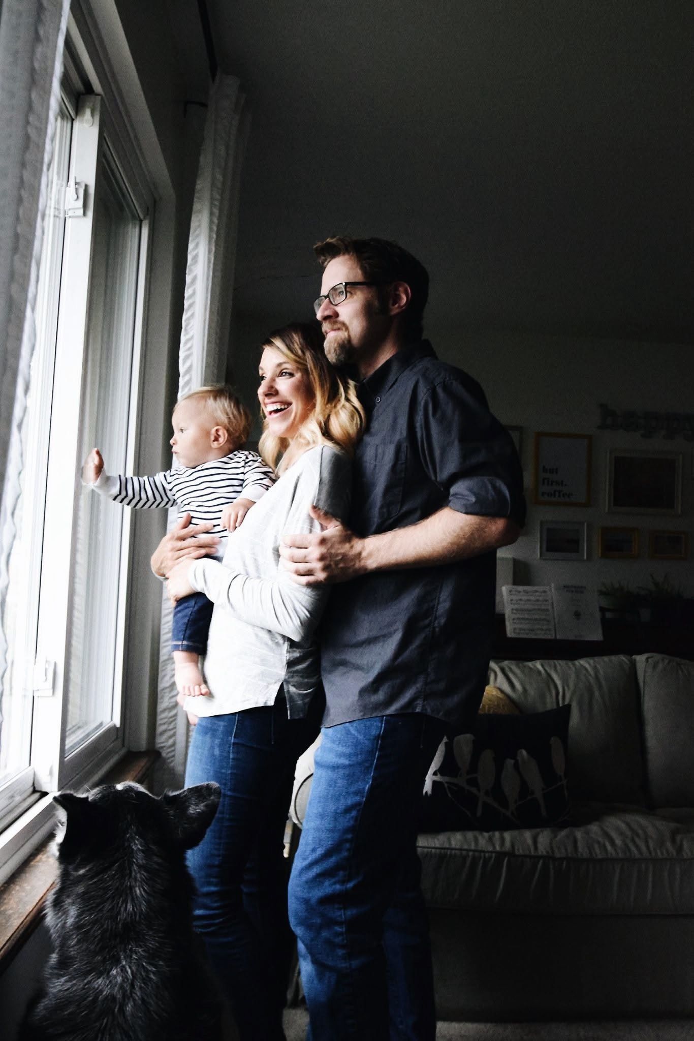 A family is standing in front of a window looking out.