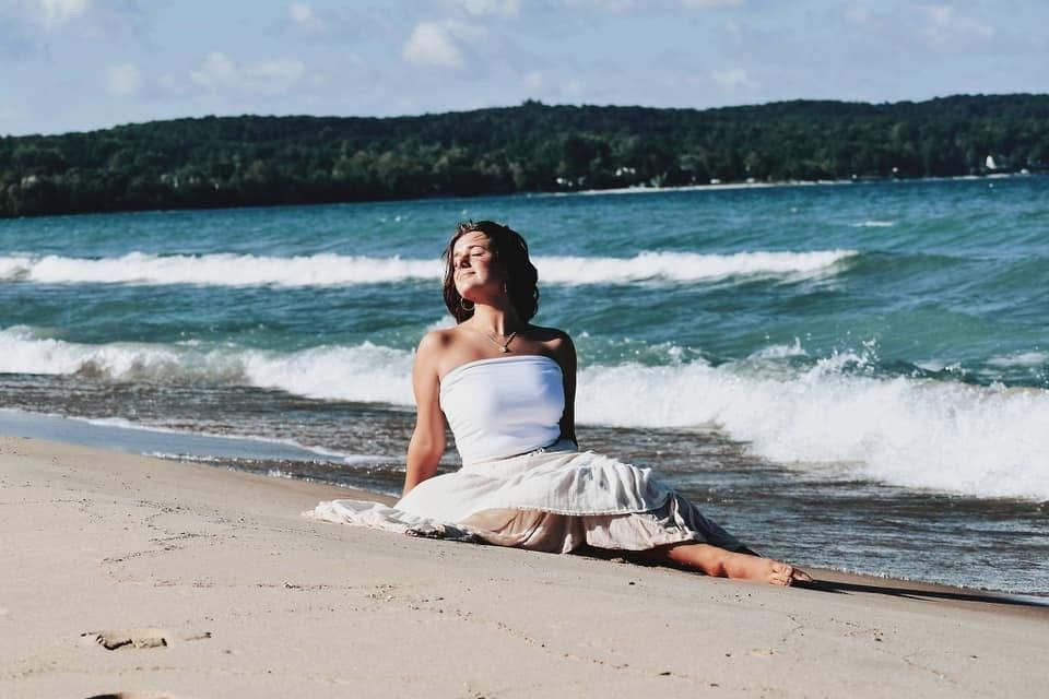 A woman is sitting on the beach looking at the ocean.