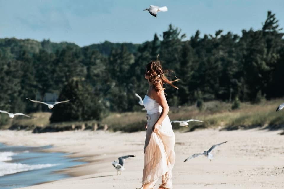 A woman is walking on a beach with seagulls flying around her.