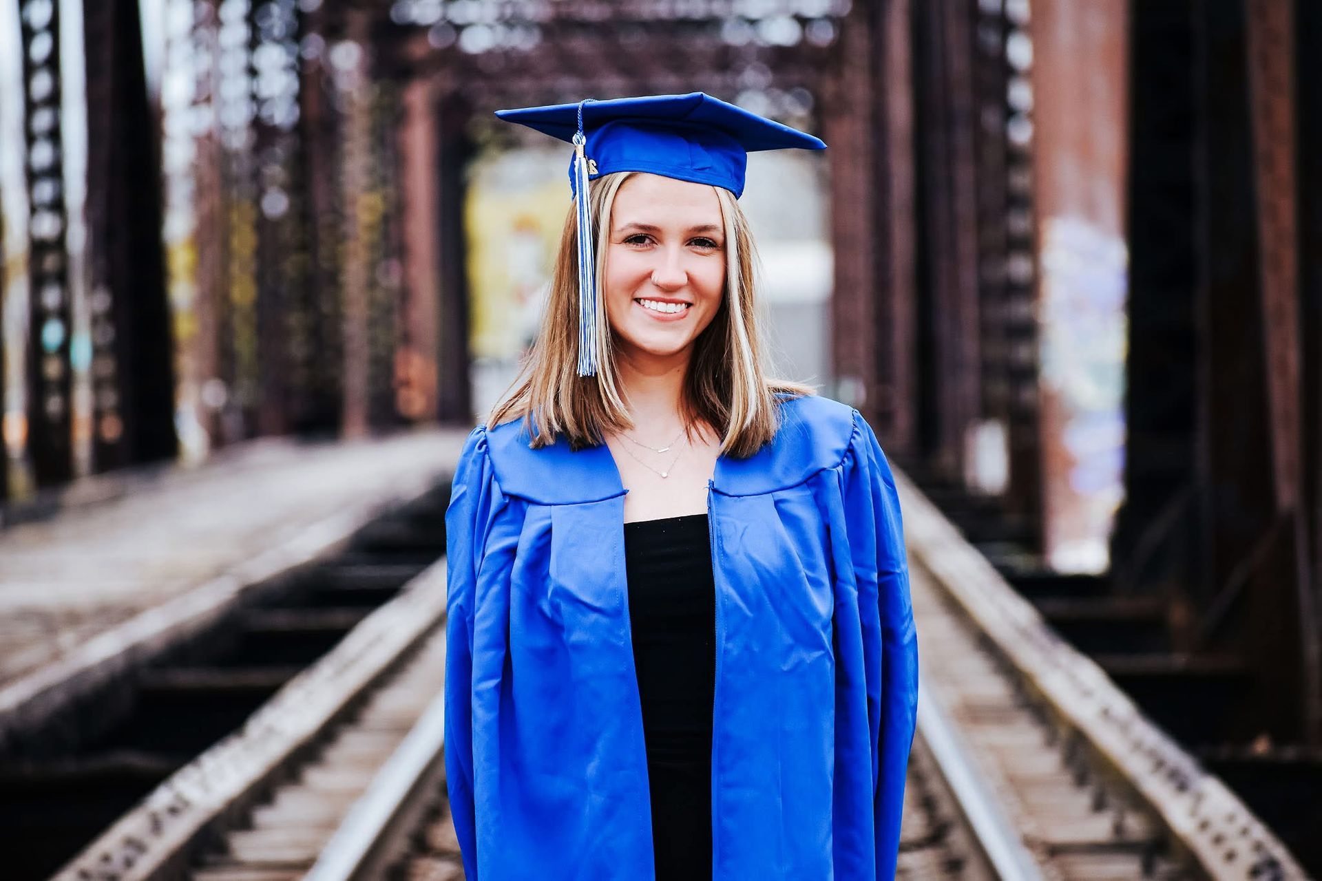 A woman in a graduation cap and gown is standing on train tracks.