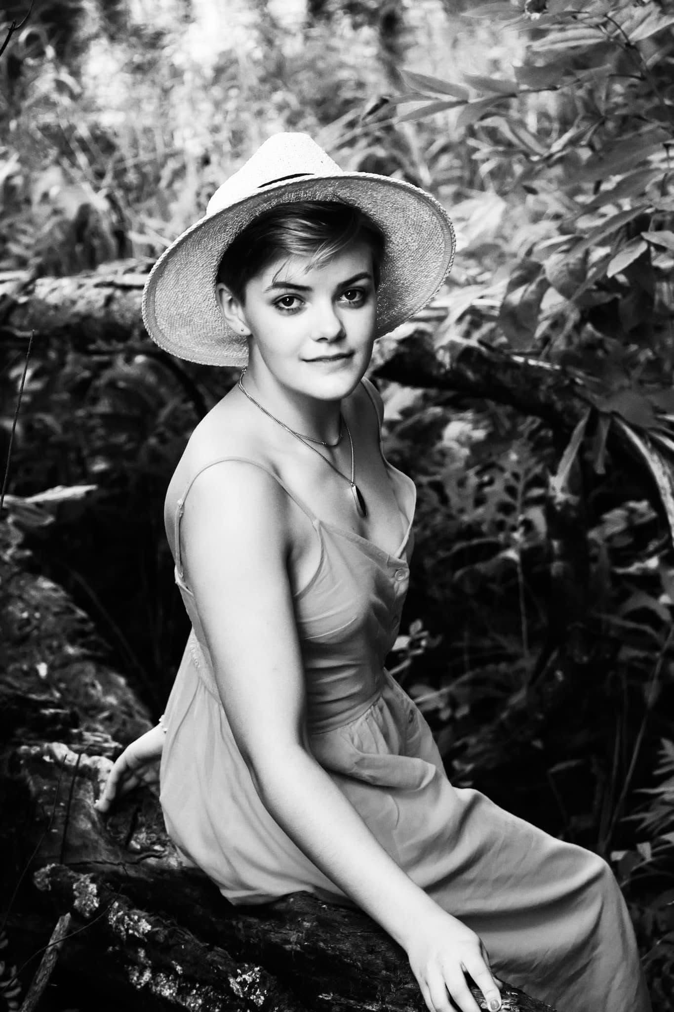 A woman in a dress and hat is sitting on a rock in the woods.