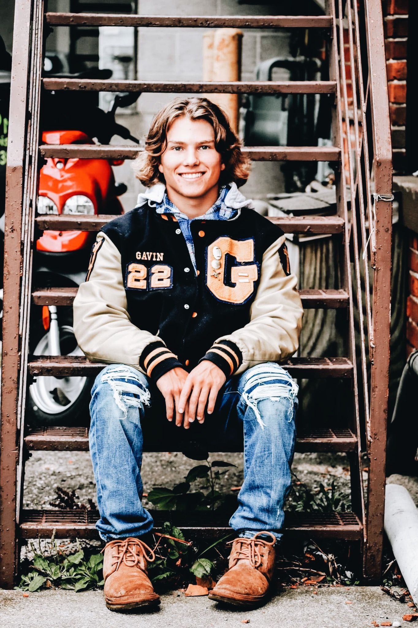 A young man in a varsity jacket is sitting on a set of stairs.