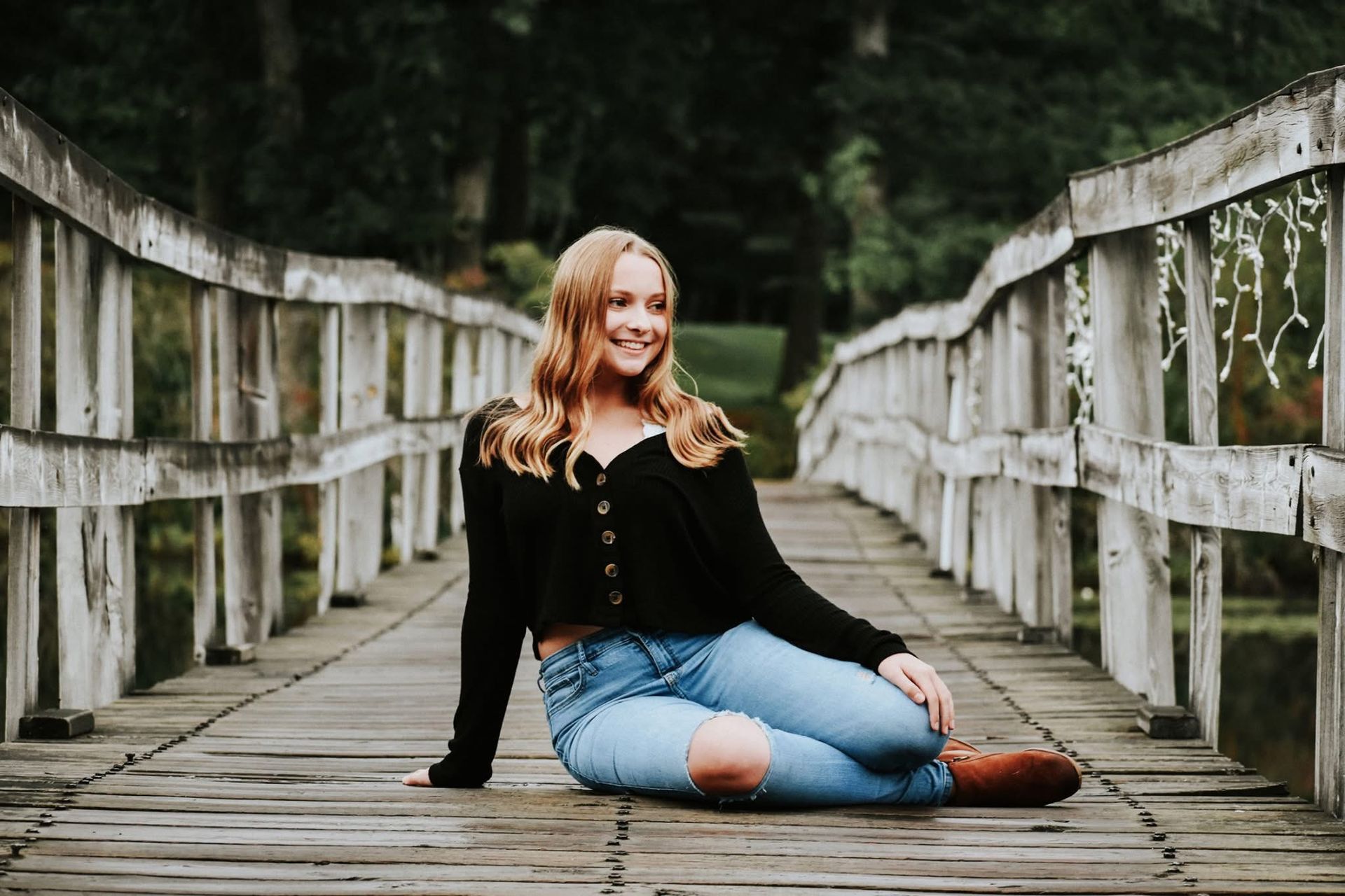 A young woman is sitting on a wooden bridge.