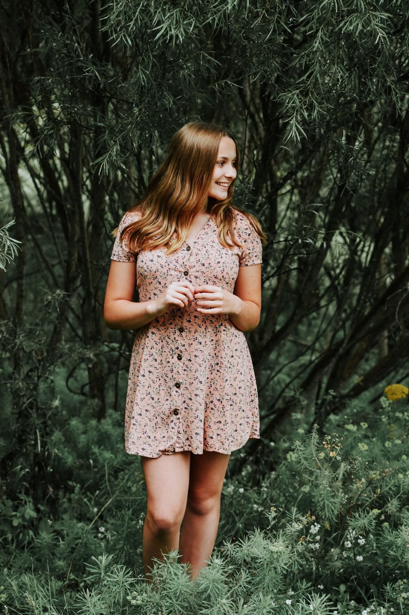 A woman in a pink dress is standing in the middle of a forest.