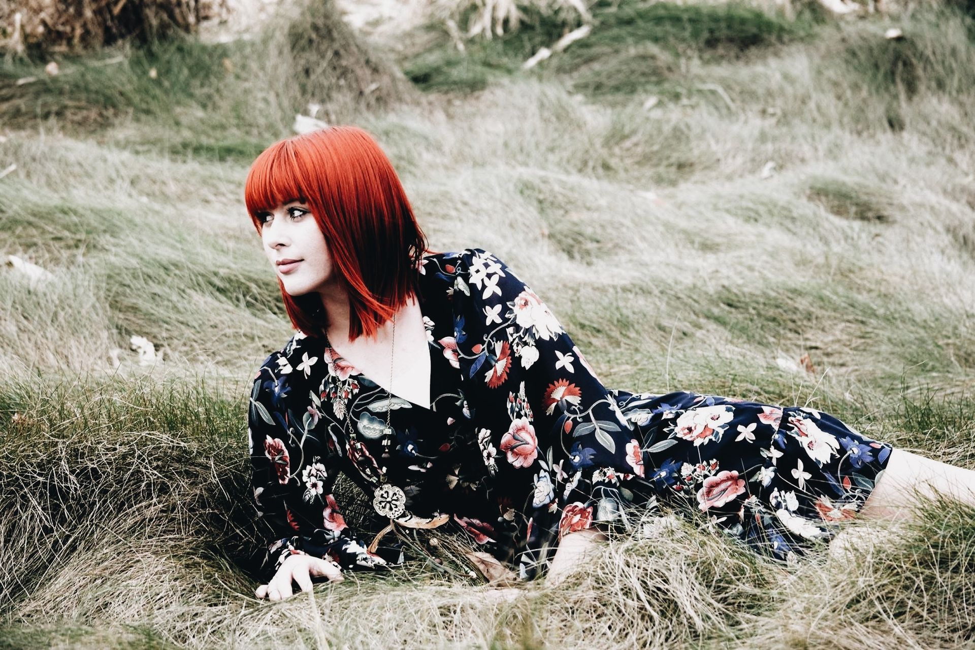 A woman in a floral dress is laying in the grass.