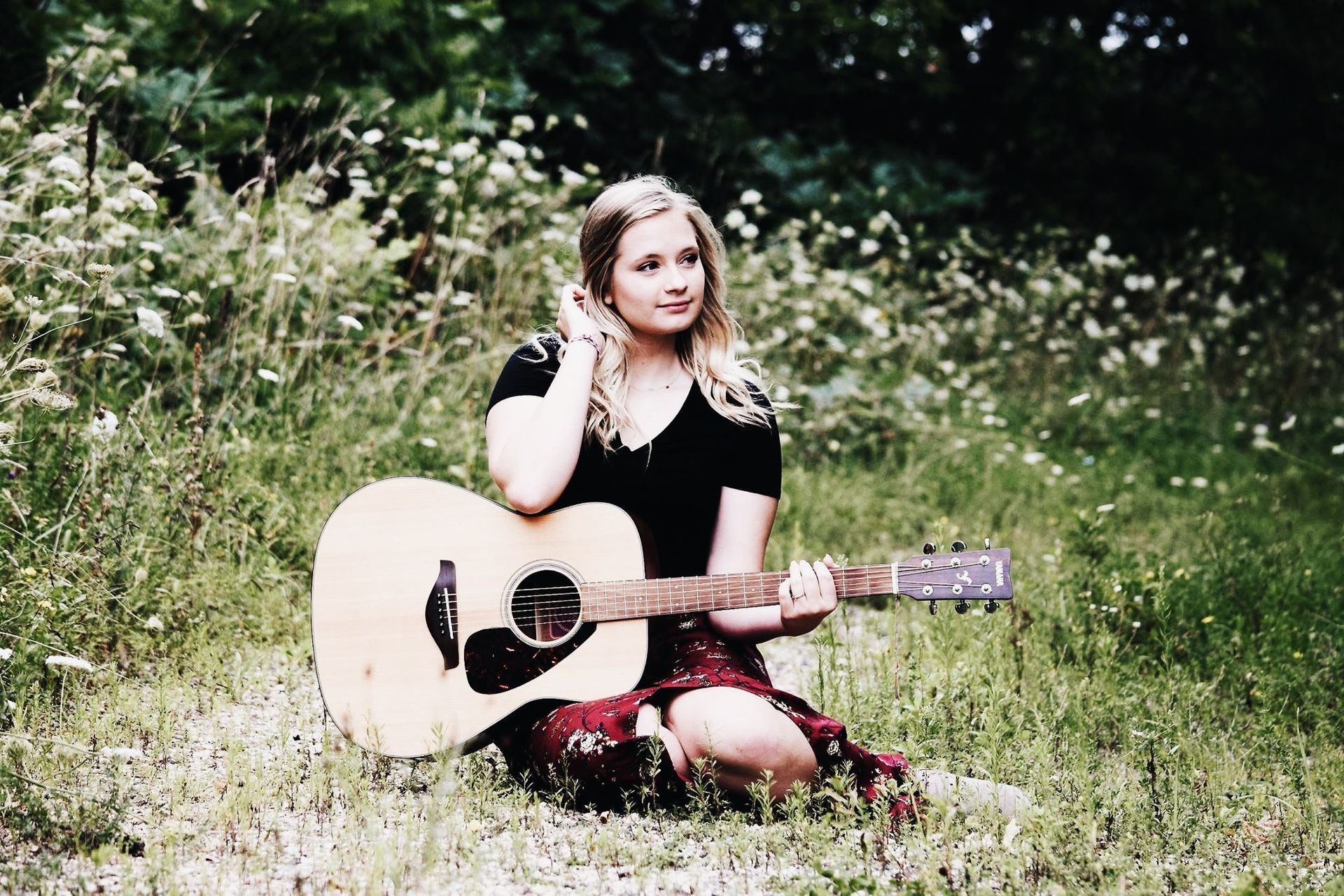 A woman is sitting in the grass holding an acoustic guitar.