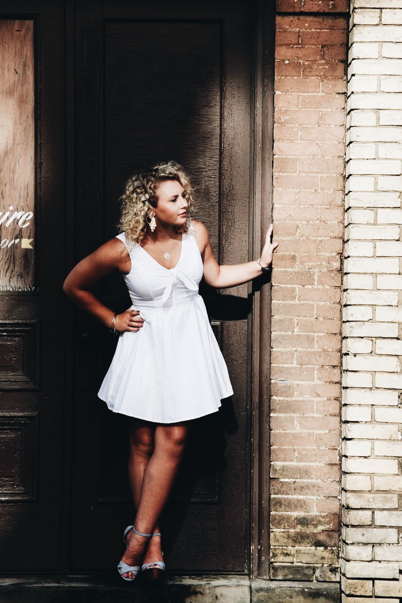 A woman in a white dress is standing in front of a brown door.