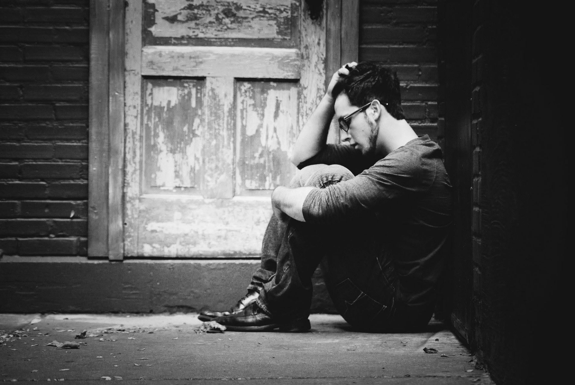 A man is sitting on the ground in front of a door with his head in his hands.