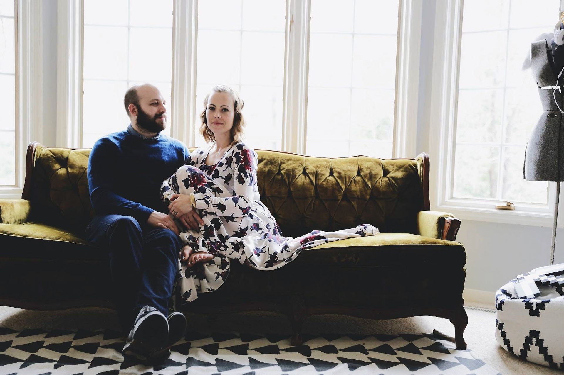 A man and a woman are sitting on a couch in front of a window.