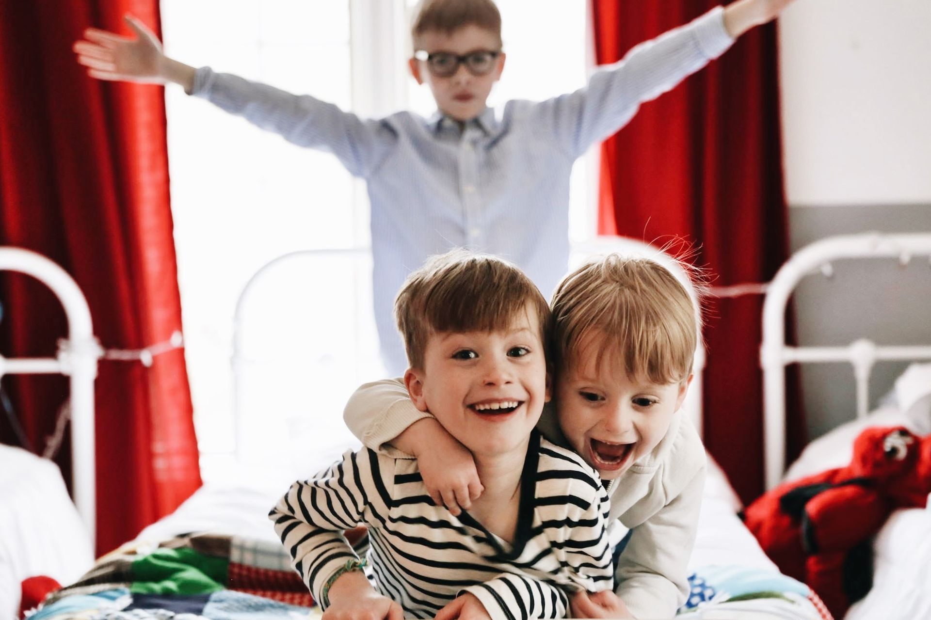 Three young boys are sitting on a bed with their arms outstretched.