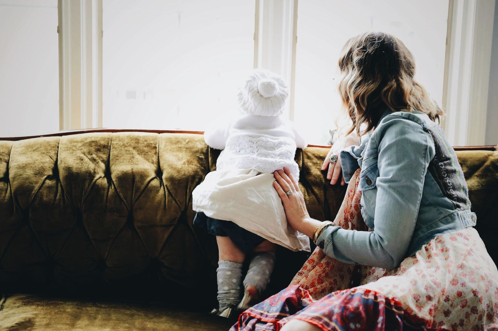 A woman and a baby are sitting on a couch looking out a window.