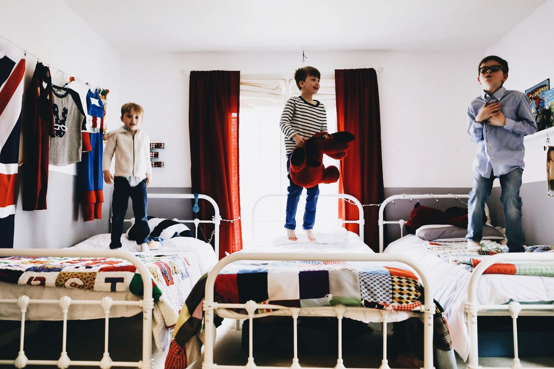 Three boys are jumping on beds in a bedroom.