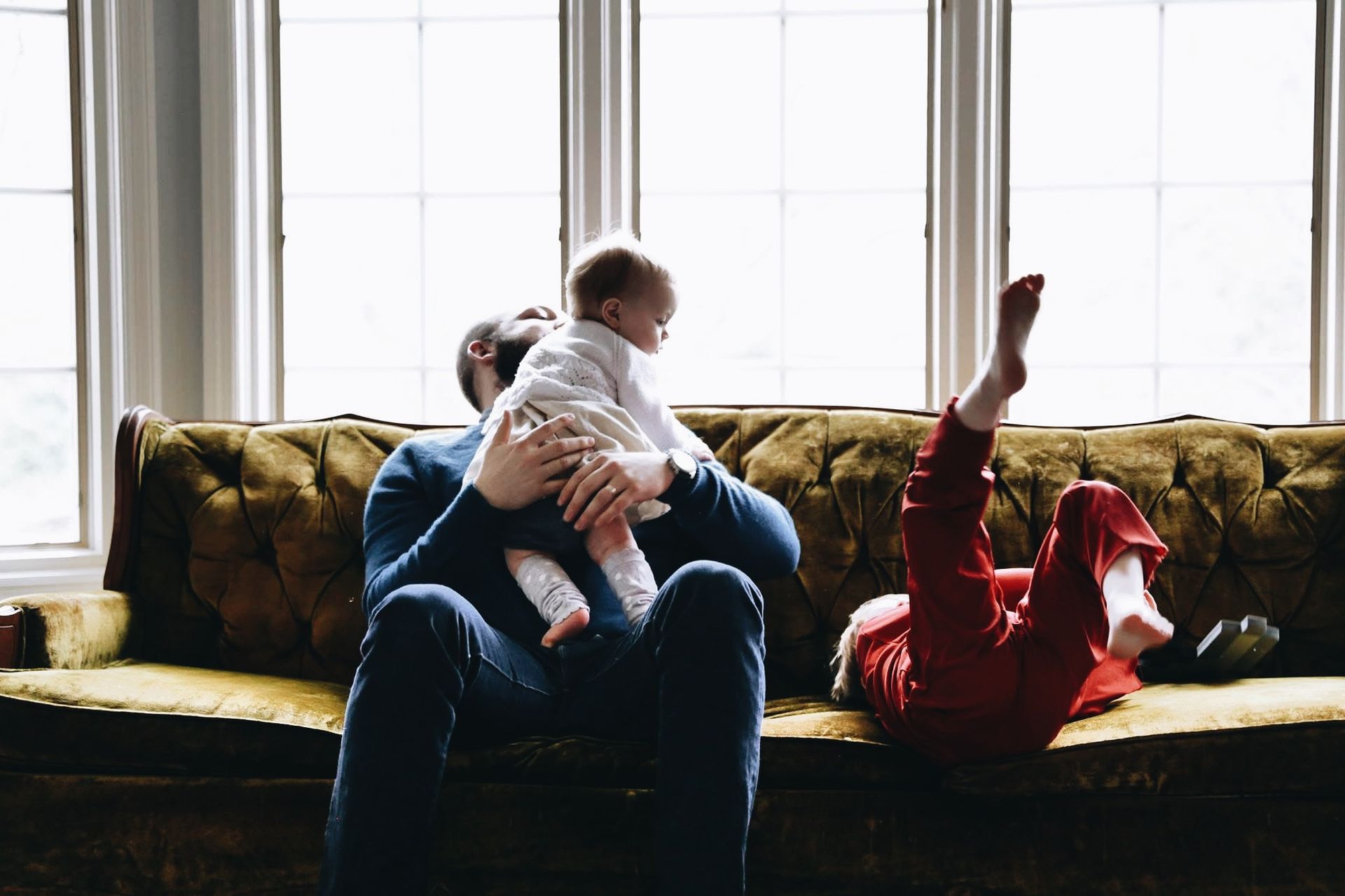 A man is sitting on a couch holding a baby and a woman is laying on the floor.