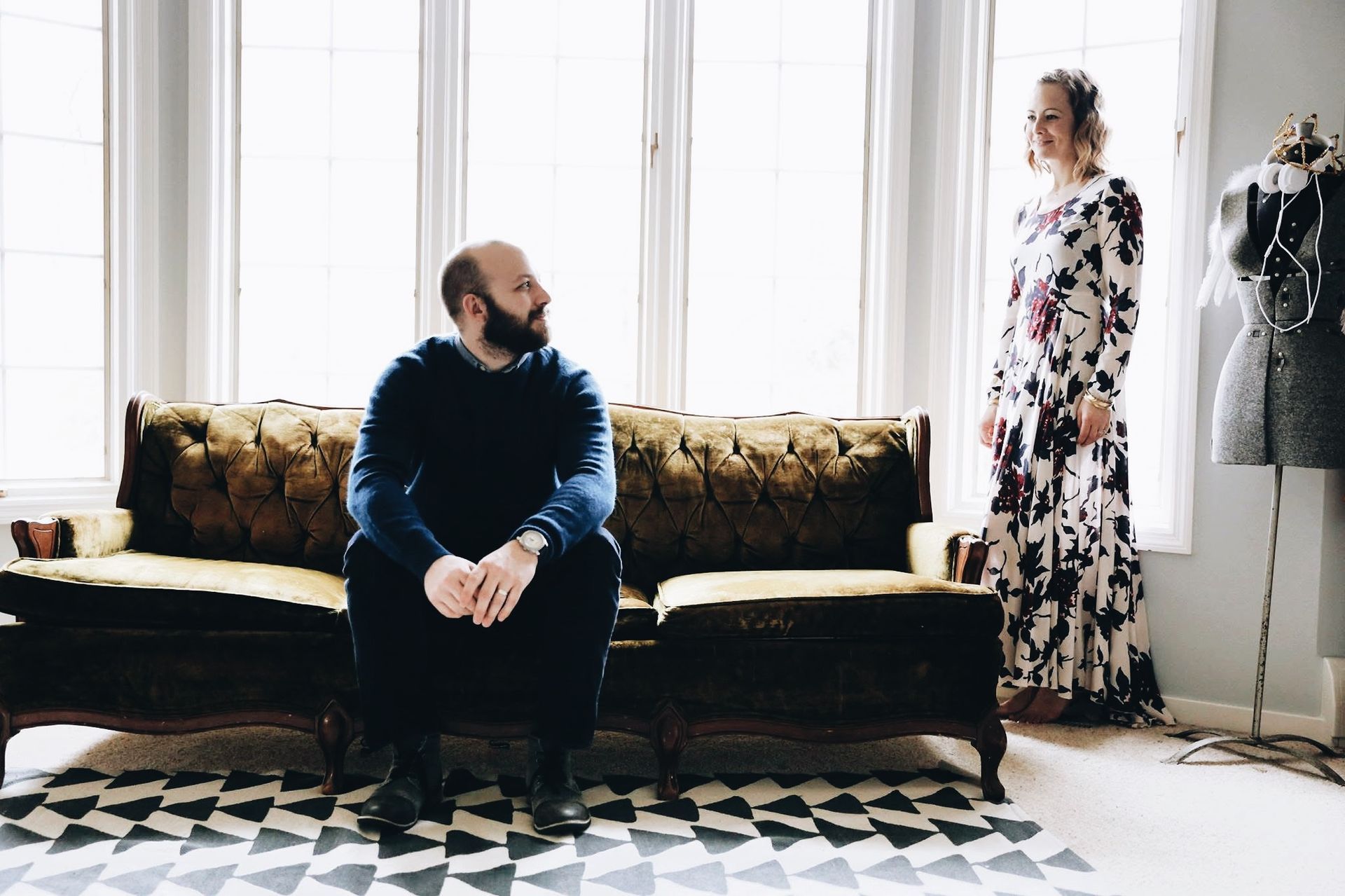 A man is sitting on a couch next to a woman in a dress.