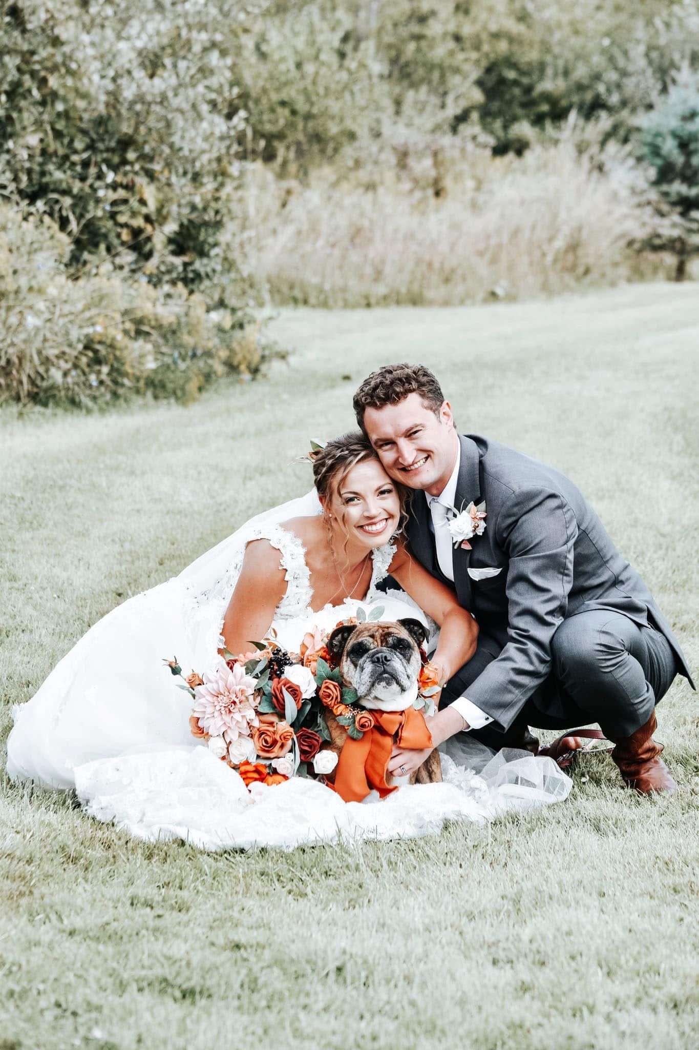 A bride and groom are posing for a picture with their dog.