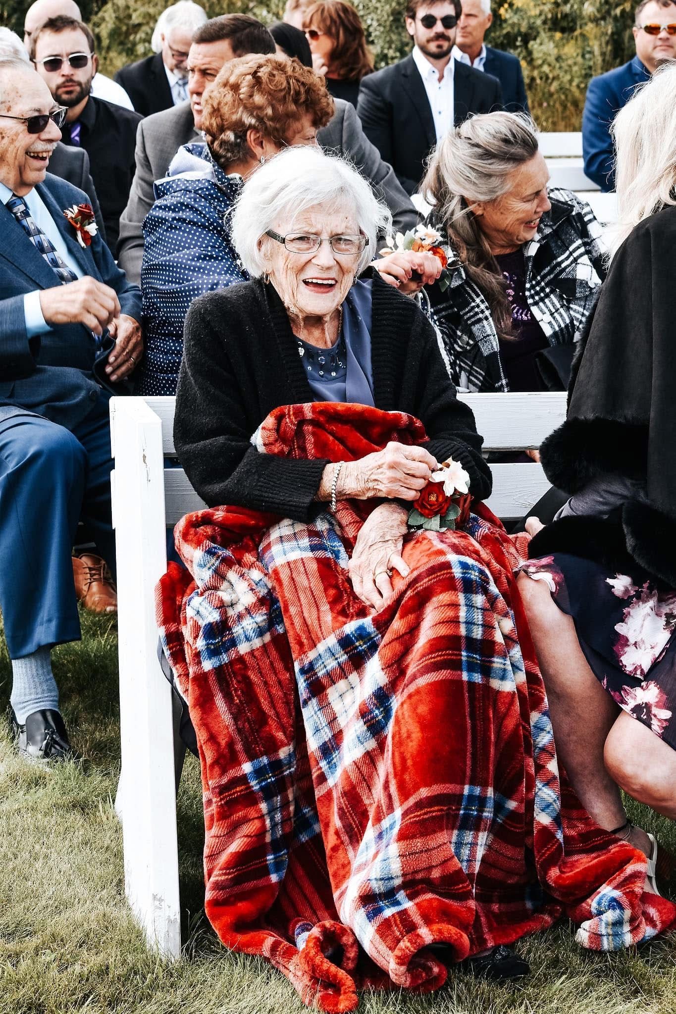A woman is sitting on a bench wrapped in a red and blue plaid blanket.