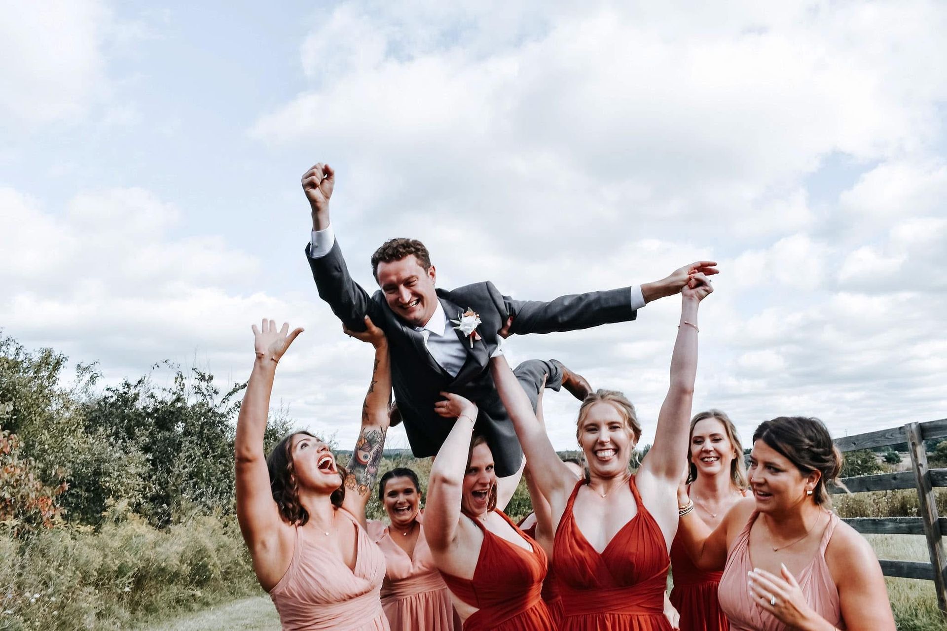 A bride and groom are being lifted in the air by their bridesmaids.