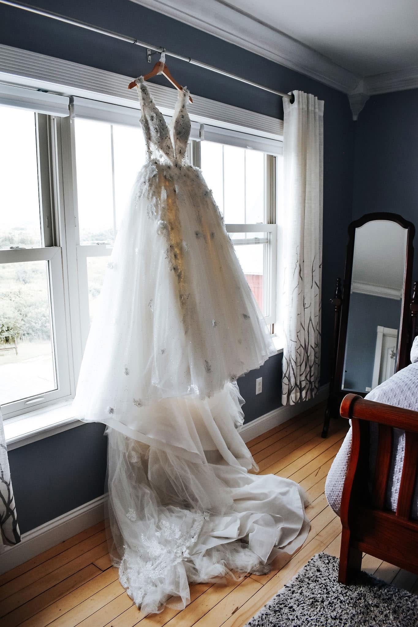 A wedding dress is hanging on a hanger in a bedroom.