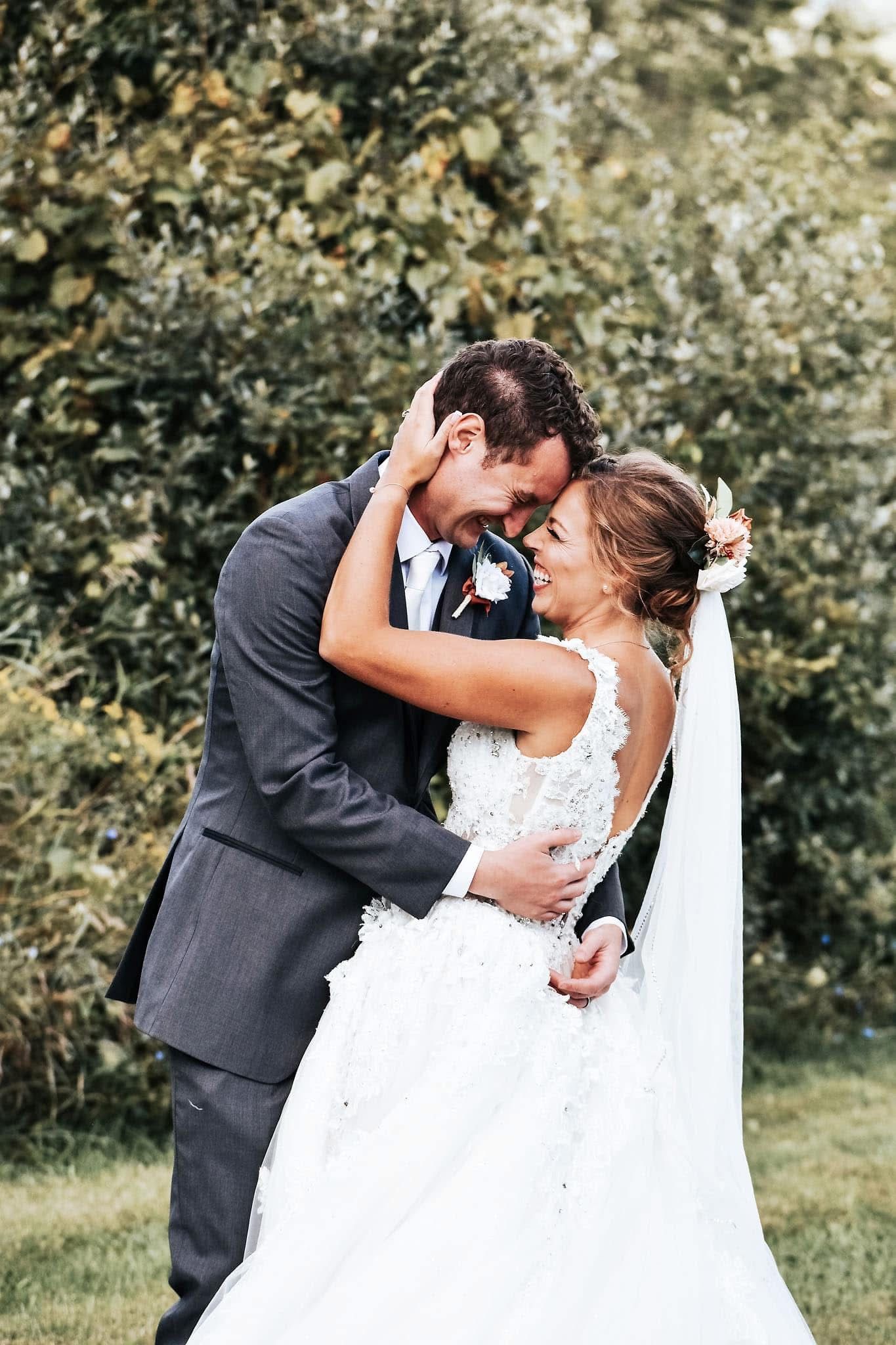 A bride and groom are hugging each other in a field.