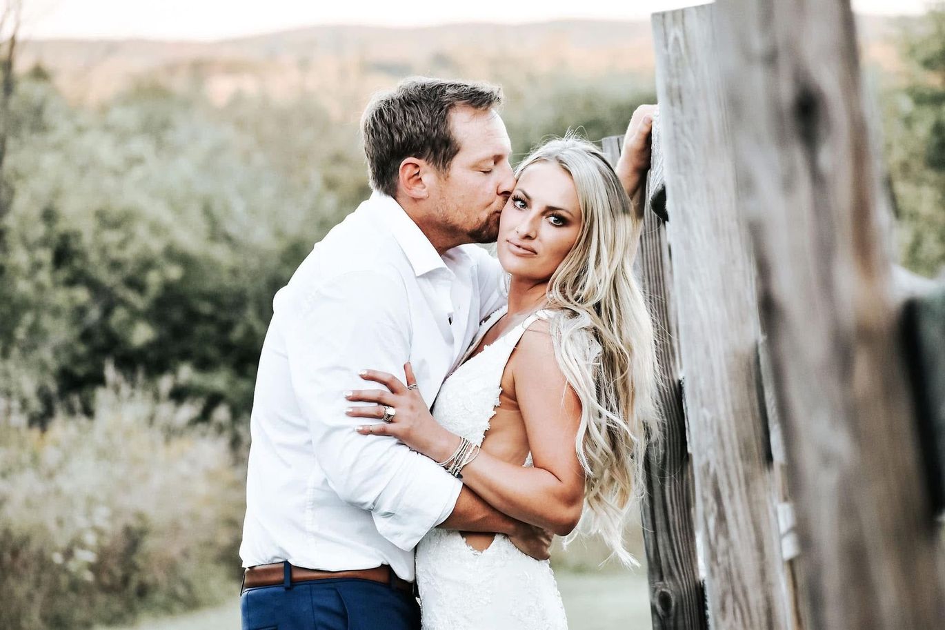 A man is kissing a woman on the cheek while standing next to a wooden fence.