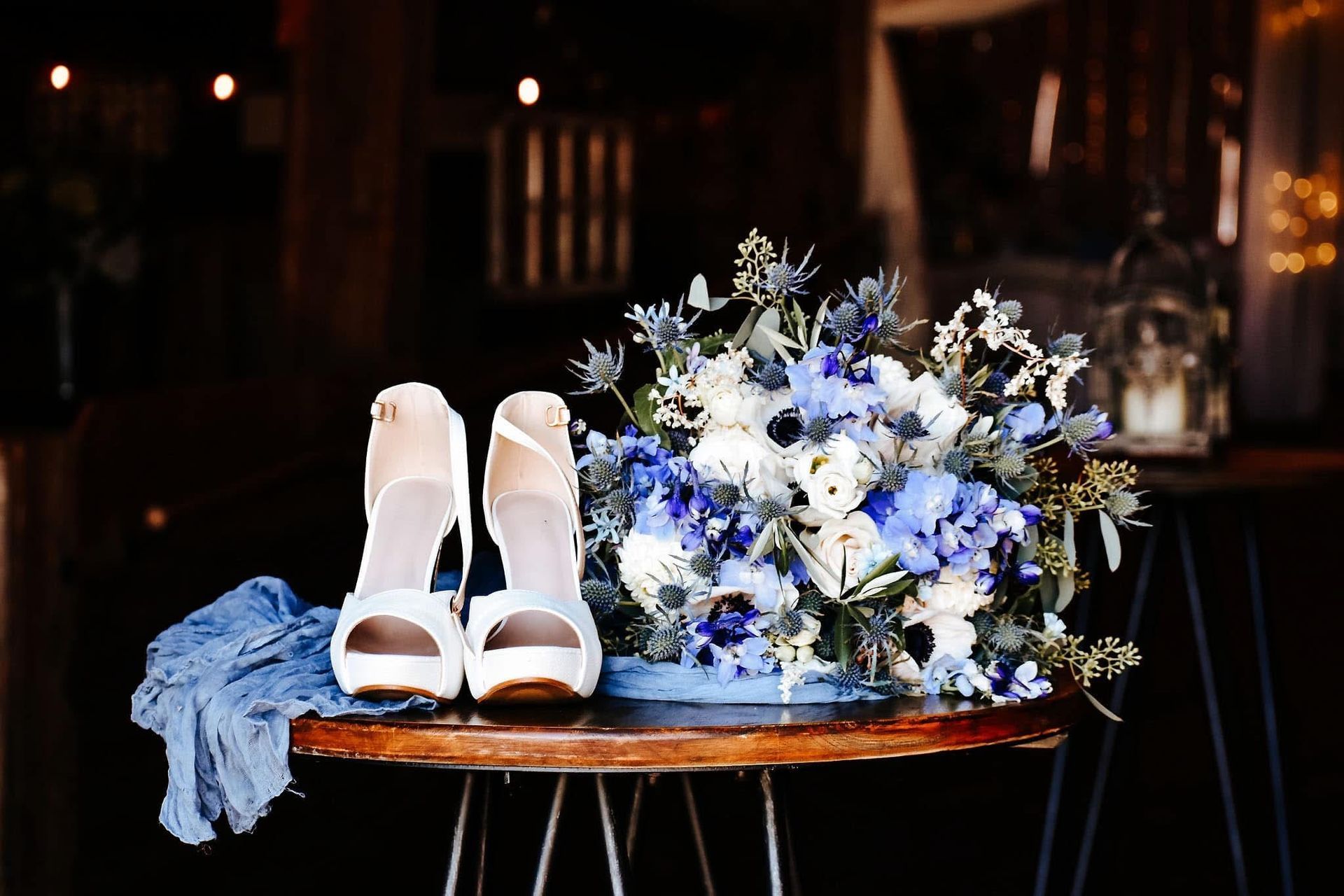 A pair of white shoes and a bouquet of blue and white flowers are on a table.