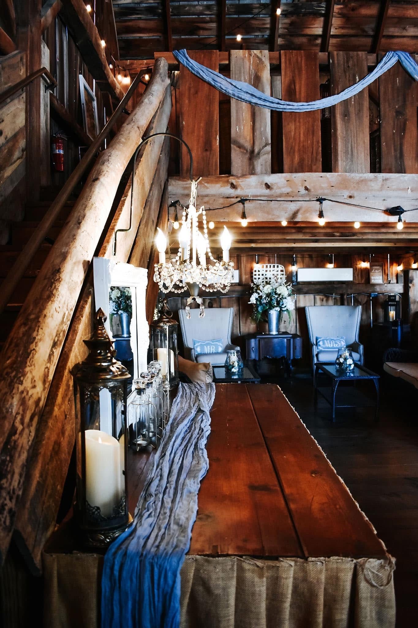 A wooden table with candles and lanterns on it in a barn.
