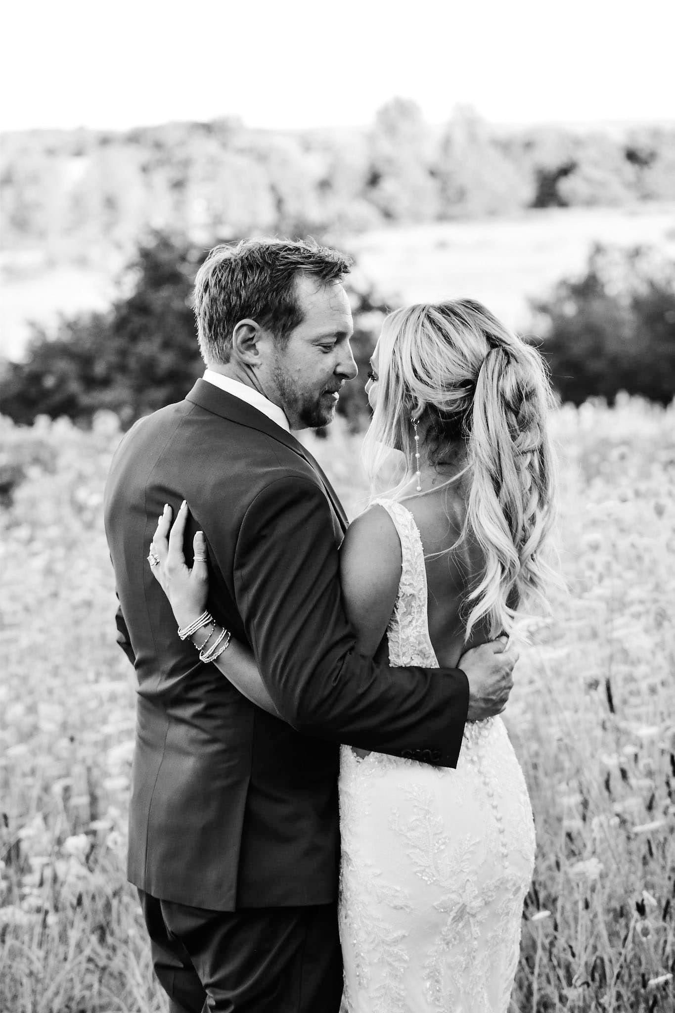 A black and white photo of a bride and groom hugging in a field.