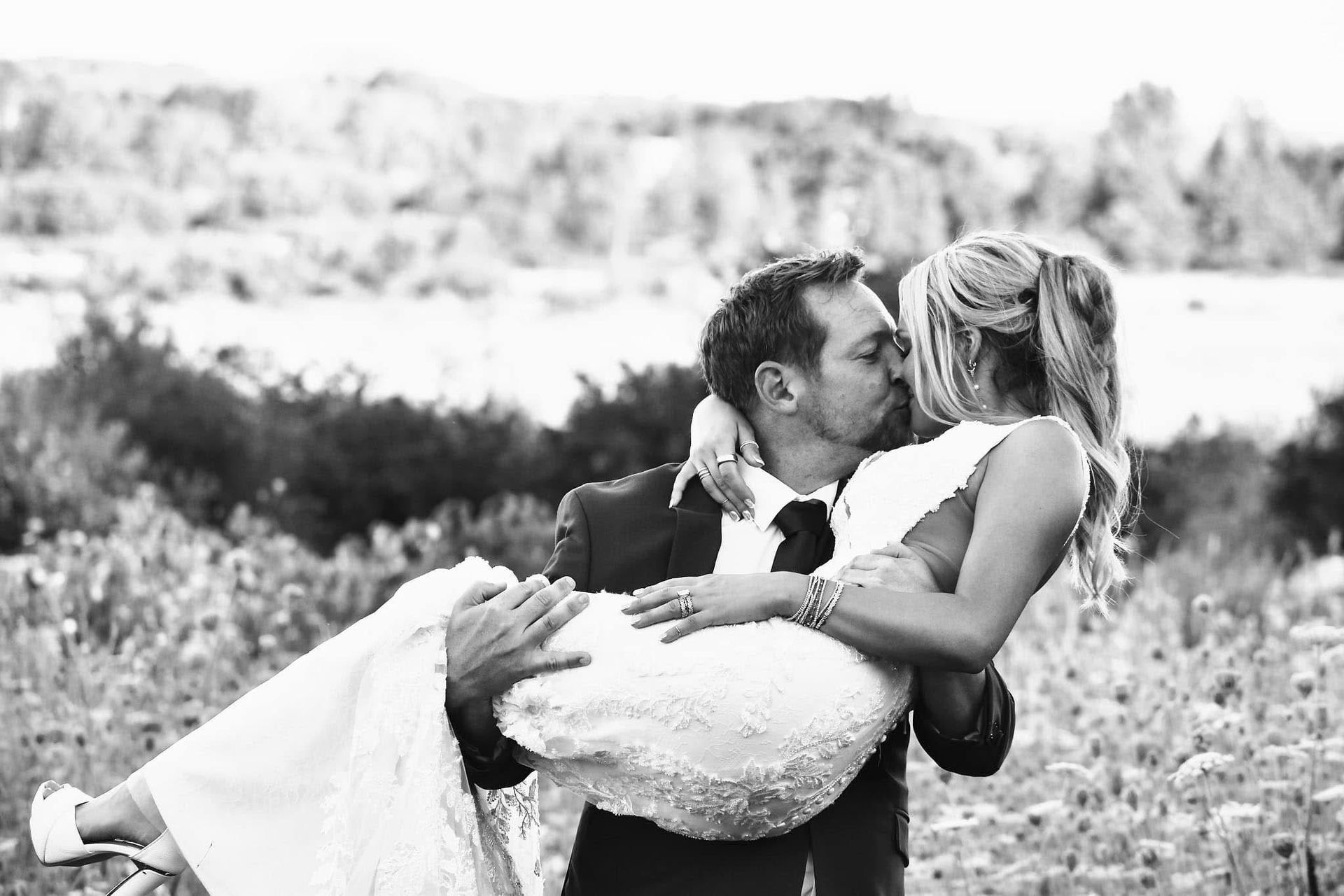 A man is carrying a bride in his arms and kissing her.