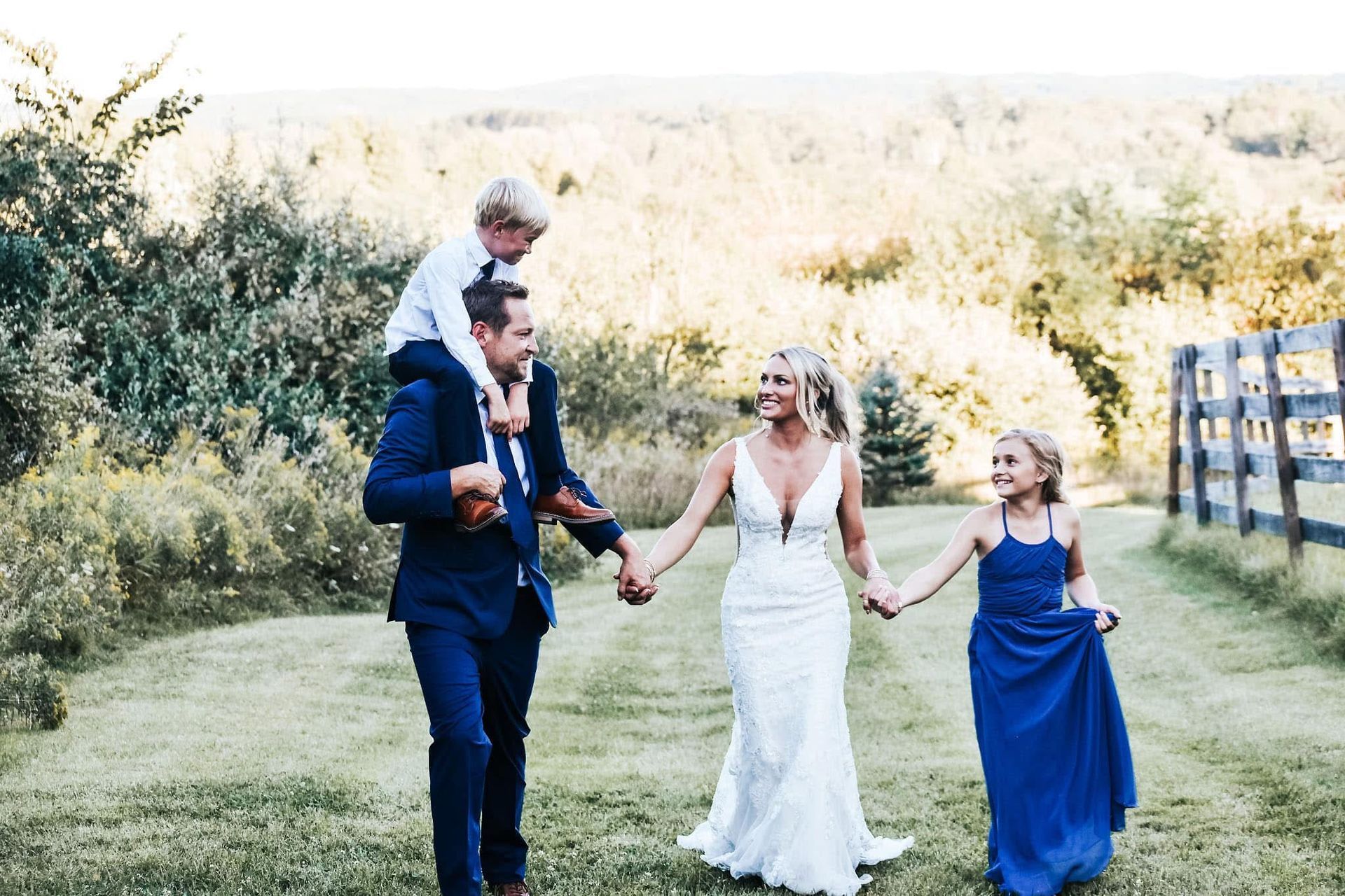 A bride and groom are holding hands with their children on their shoulders.