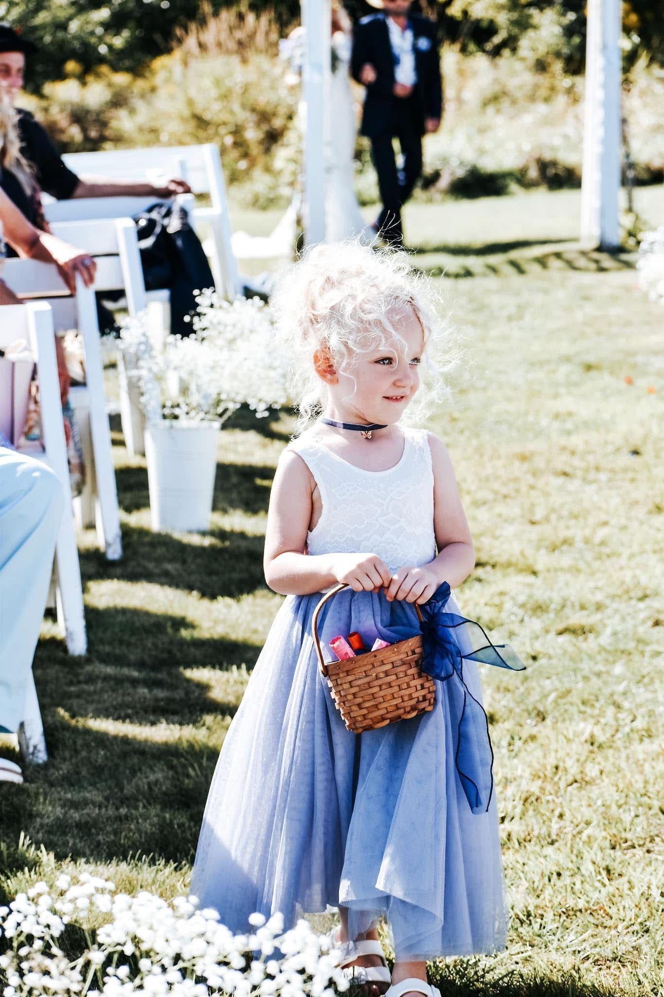 A little girl in a blue dress is holding a basket of flowers.