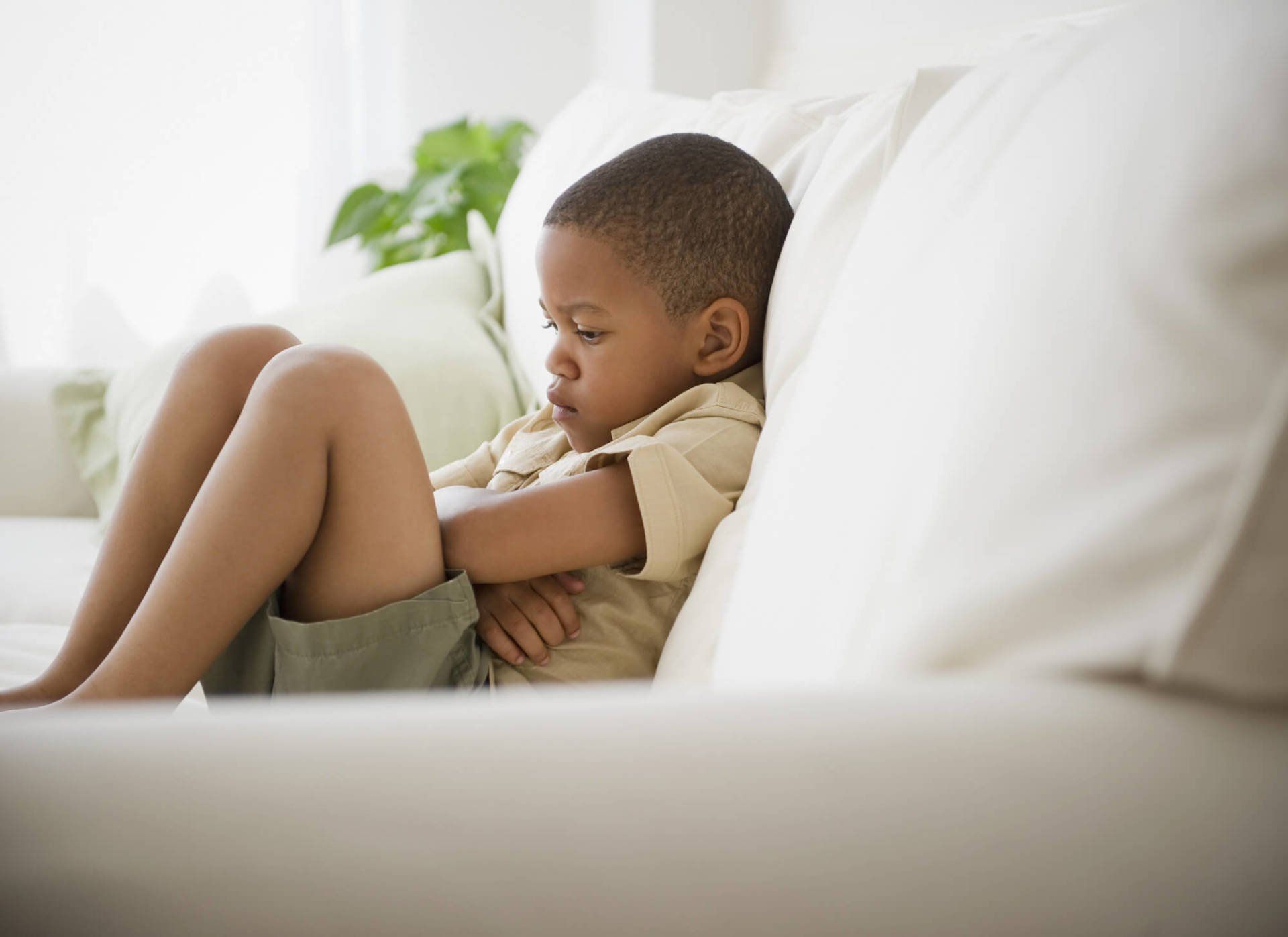 Young boy looking sad sat on a sofa