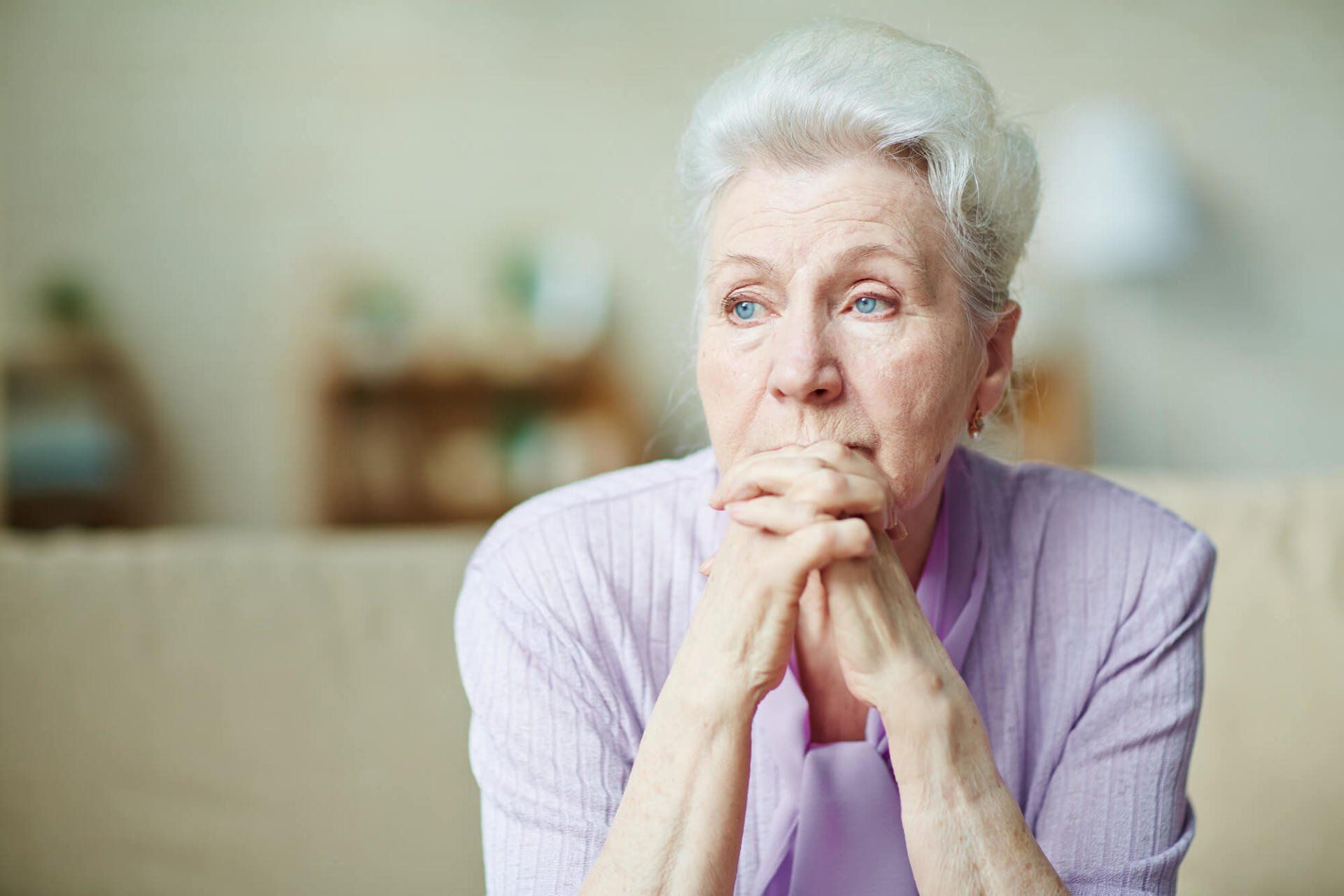 Older female with her chin resting on her hands. She looks deep in thought.