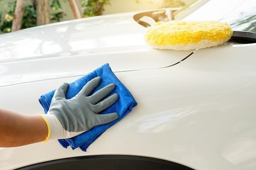 A person is cleaning a white car with a blue towel and sponge.