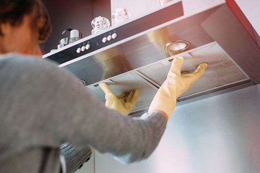 A woman wearing yellow gloves is cleaning a hood in a kitchen.