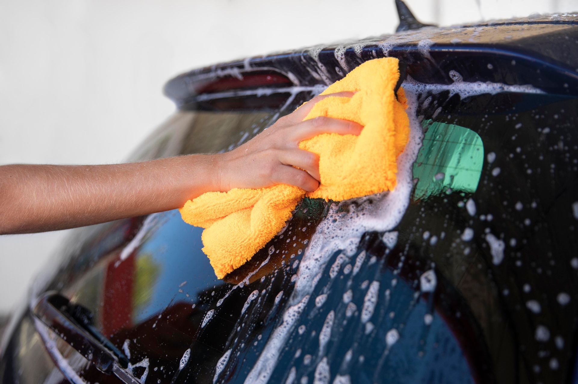 A person is washing a car with a yellow towel.