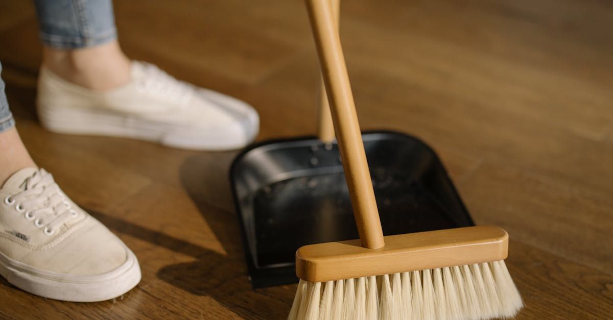 A person is cleaning the floor with a broom and dustpan.