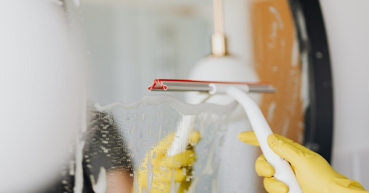 A person wearing yellow gloves is cleaning a window with a squeegee.
