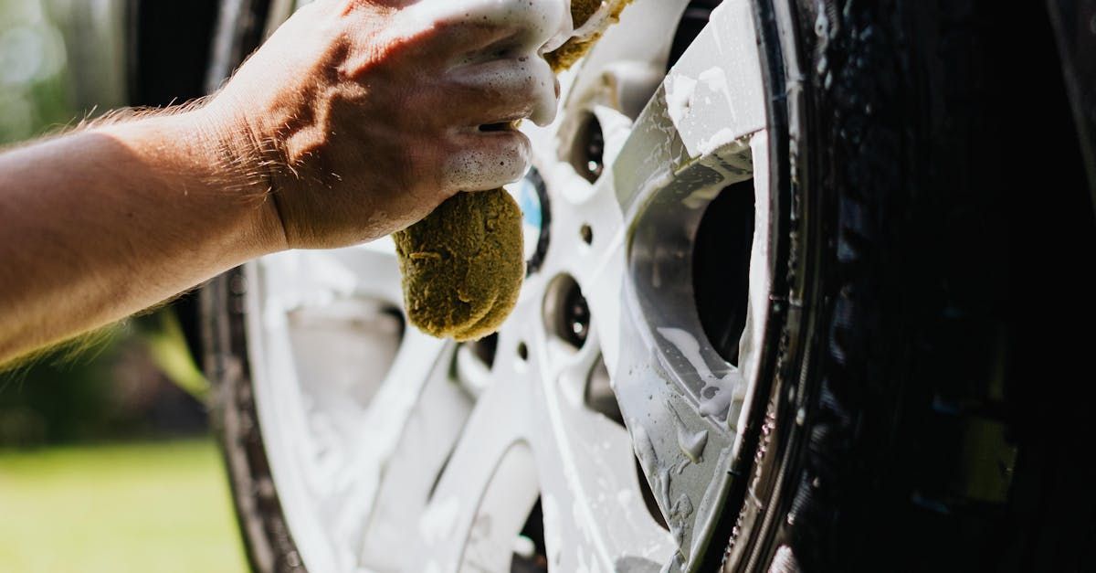 A person is washing a car wheel with a sponge.