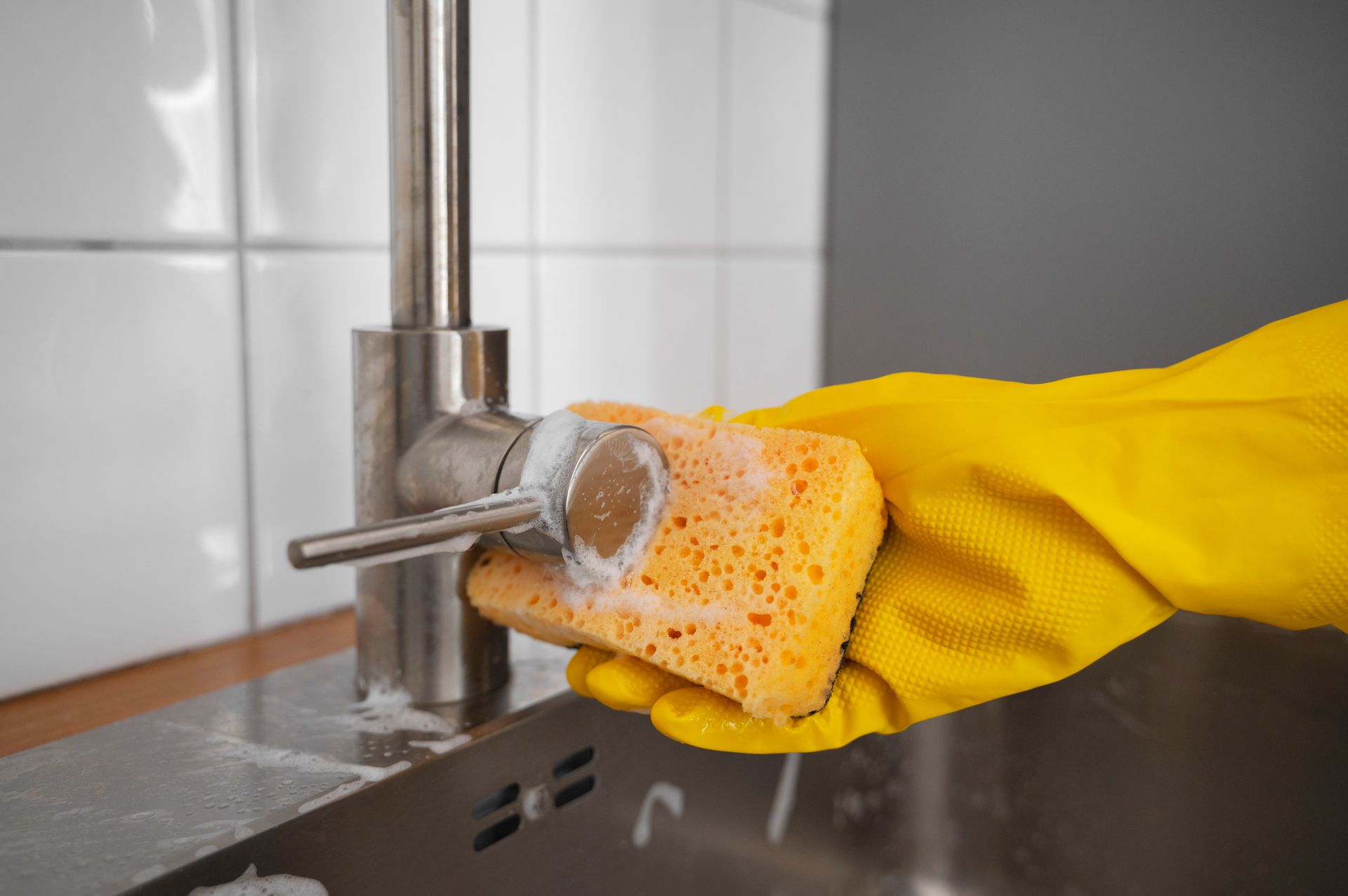 A person wearing yellow gloves is cleaning a sink with a sponge.