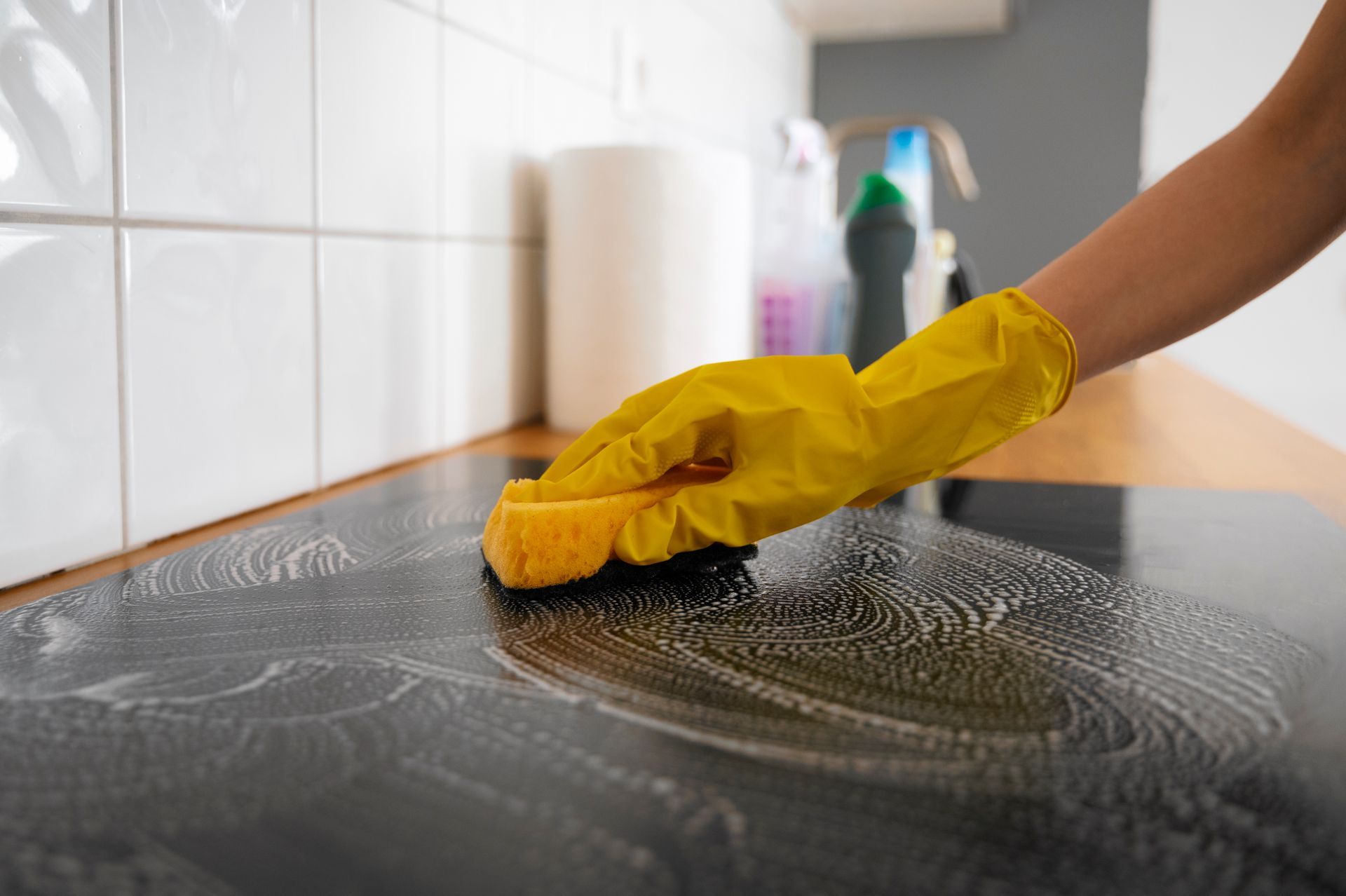 A person wearing a yellow glove is cleaning a counter with a sponge.