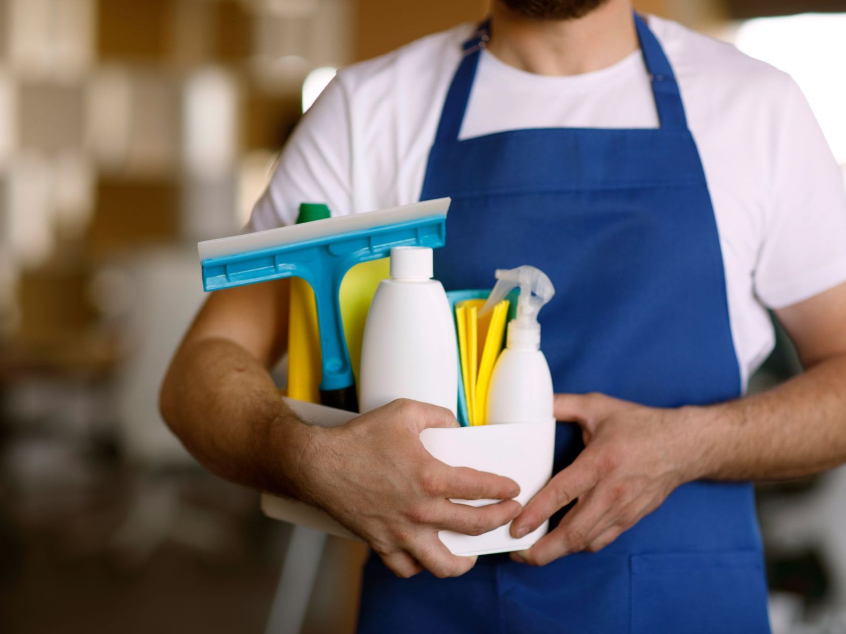 A man in an apron is holding a bowl of cleaning supplies.